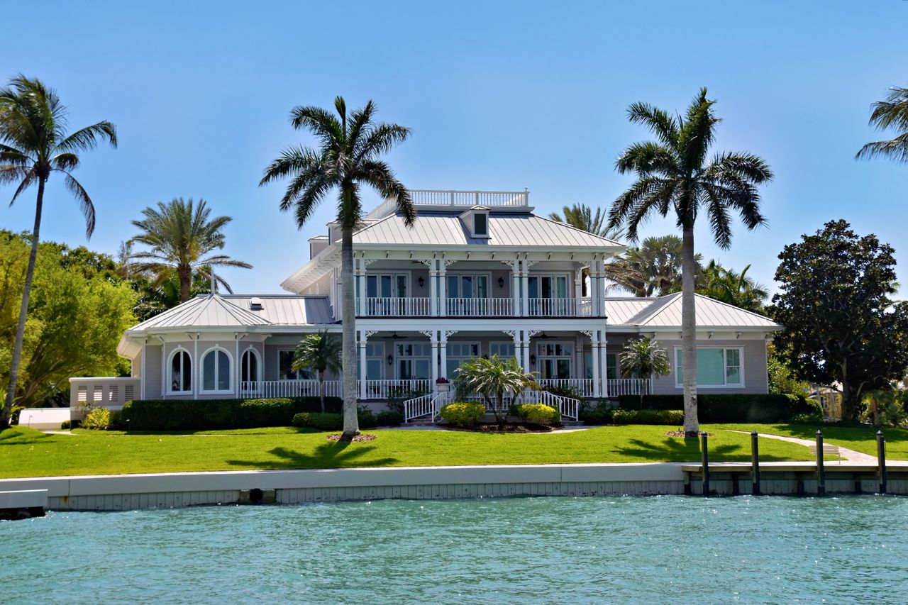 Elegant waterfront villa with palm trees and lush greenery, ideal for luxury living.